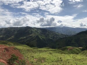 Lush green hills and mountains under a partly cloudy blue sky.