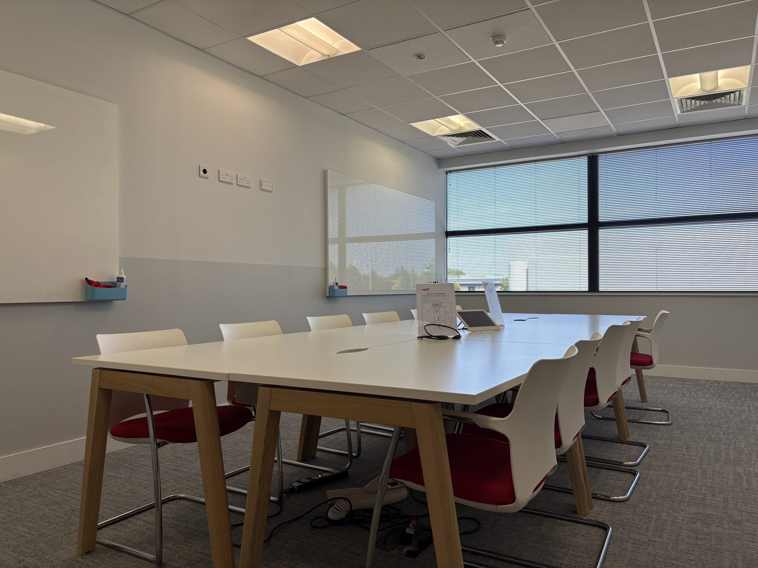Modern conference room with a long table, white chairs, whiteboards, and large windows with blinds.