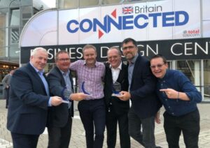 Six men smiling and holding awards in front of a "Britain Connected" sign at a business event.