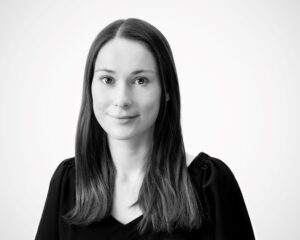 Black and white portrait of a person with long hair, wearing a dark top, smiling softly against a plain background.