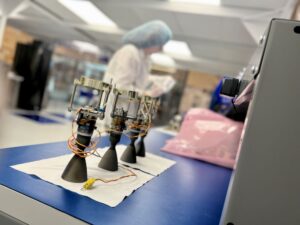 Small rocket engines on a table with a person in protective clothing working in the background.