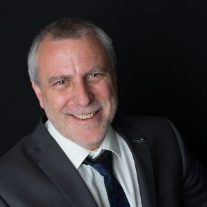 Smiling man in a suit and tie against a dark background.