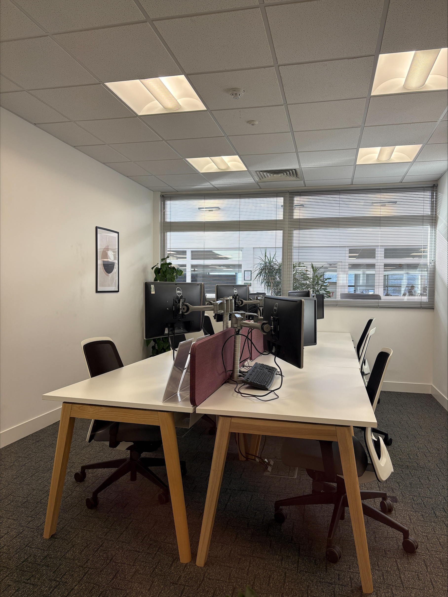 A modern office with desks, computer monitors, chairs, and large windows letting in natural light.