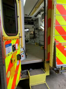 Open ambulance with visible interior medical equipment and reflective yellow-red stripes on the doors.