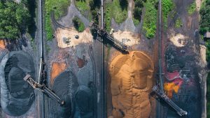 Aerial view of industrial machinery sorting large piles of coal and sand, with surrounding greenery.