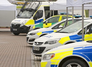 Police vehicles with blue and yellow markings parked in a row, including cars and a van.