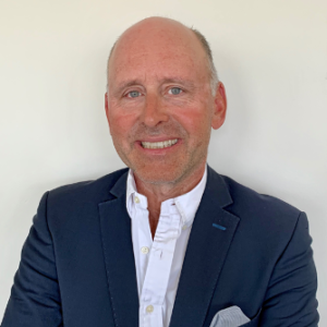 Smiling man in a dark blazer and white shirt against a plain background.