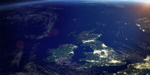 Aerial view of the UK and Ireland at night, city lights visible against the dark ocean and land.