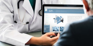 Doctor showing a medical website on a tablet to a patient, with a stethoscope visible.