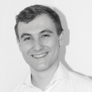 Black and white photo of a person smiling, wearing a white shirt against a plain background.