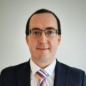 Person wearing glasses and a suit with a colorful striped tie, smiling slightly against a plain background.