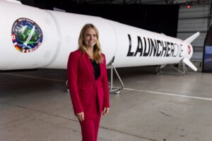 Person in a red suit standing in front of a Launch Canada rocket in a hangar.