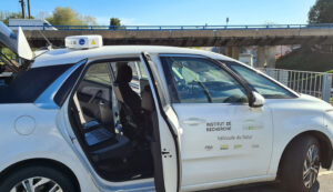 White research vehicle with open doors, labeled "Institut de Recherche Vedecom," parked near a bridge.