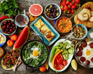 A colorful brunch spread with fruits, vegetables, eggs, pastries, and various small dishes on a wooden table.