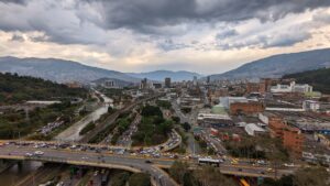 Aerial view of Medellín cityscape with mountains, cloudy sky, and busy roads.