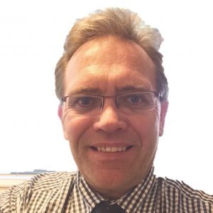 Smiling man wearing glasses and a checkered shirt with a tie against a white background.