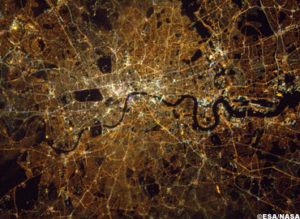 Aerial view of a city at night with illuminated streets and a winding river, showcasing urban patterns.