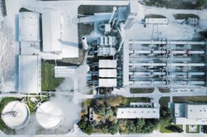 Aerial view of an industrial complex with buildings, machinery, and storage tanks emitting steam or smoke.