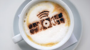 Coffee cup with frothy latte art resembling a camera icon on a white saucer with a napkin.