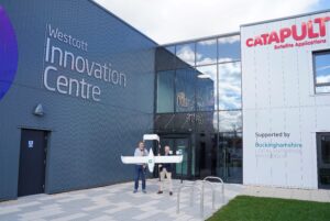 Two people holding a drone outside Westcott Innovation Centre and Catapult Satellite Applications building.