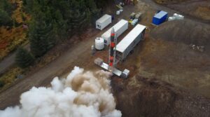 A small rocket is surrounded by smoke and steam on a launchpad in a forested area.