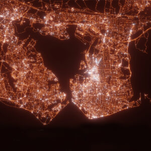 Aerial view of a cityscape at night with glowing orange lights, outlining roads and waterways.