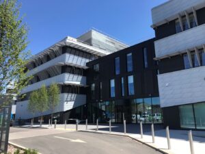 Modern multi-story building with angular design, large windows, and metal facade, under a clear blue sky.