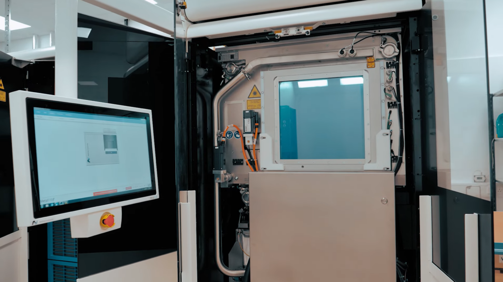 Industrial machine with a control screen and buttons, showing a window into the machine's internal components.