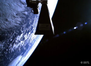 A satellite hovers in space above Earth's surface, which is partially visible on the left, with a dark sky background.