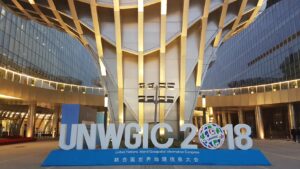 Large modern building entrance with "UNWGIC 2018" sign and globe logo; reflective surfaces and glass facade.
