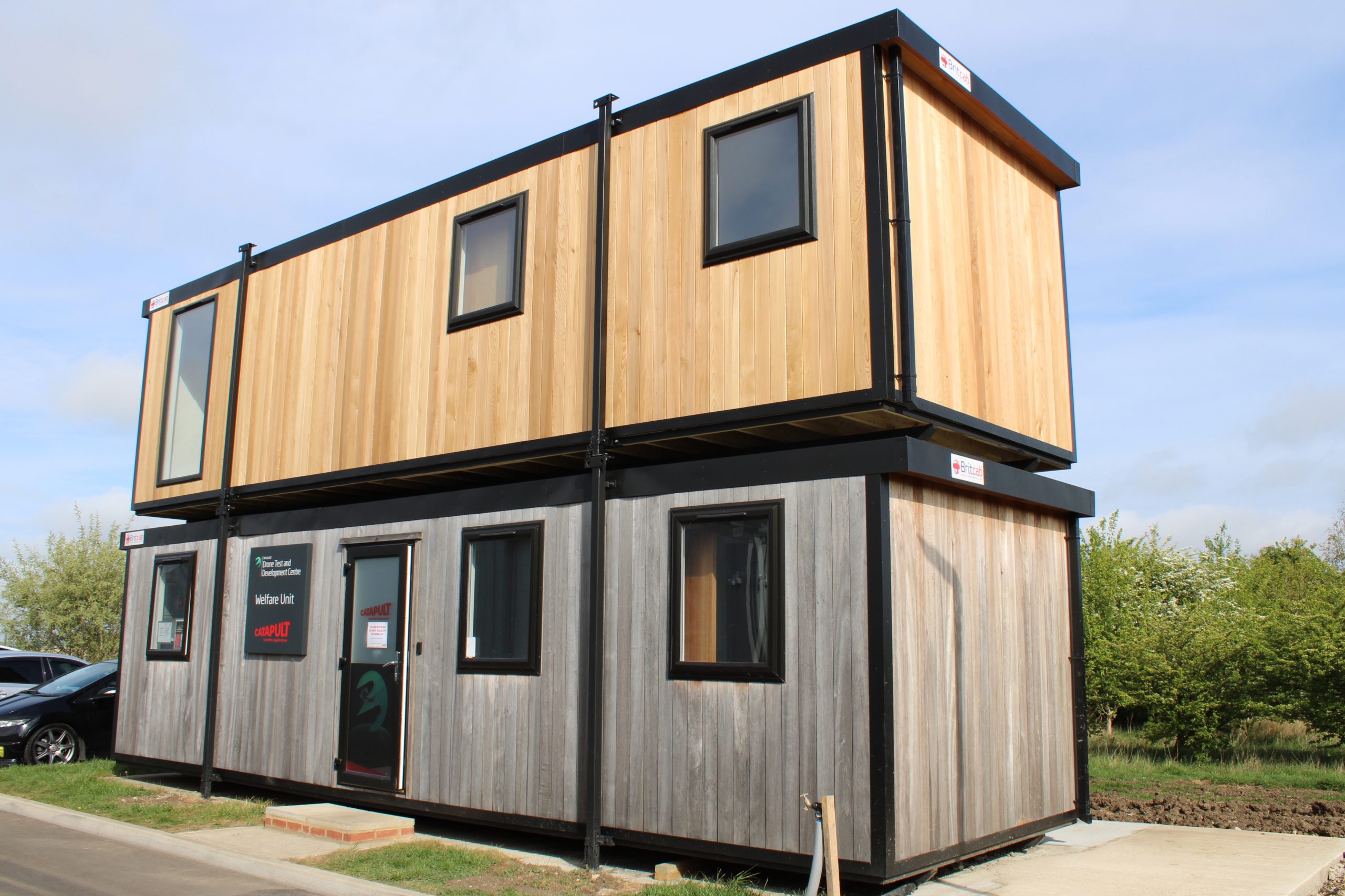 Two-story modular building with wood paneling, large windows, and a modern rectangular design.
