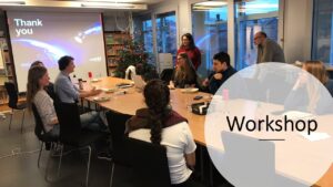 People sitting around a table in a bright room, with a presentation screen displaying "Thank you.