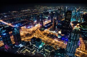 Aerial view of a vibrant cityscape at night with illuminated skyscrapers and busy roads forming a glowing network.