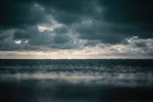 Dark, clouds over a calm sea as the horizon glows with soft light, creating a moody, serene atmosphere.