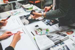 People collaborating at a table with papers, markers, photos, and a smartphone.