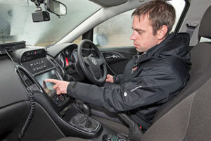 Person in a car interacting with a touch screen on the dashboard, wearing a black jacket.