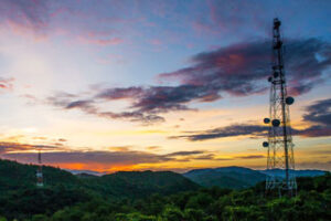 Cell towers on a lush hillside with a vibrant sunset sky above.