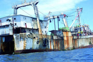 Rusty, industrial fishing boat floating on calm waters under a clear blue sky.