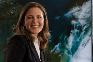 Person smiling in front of a large screen displaying a satellite image of Earth.