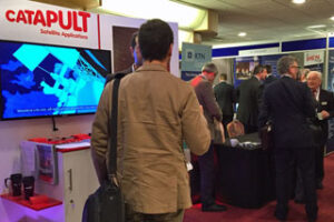 People attending a technology conference with a "Catapult Satellite Applications" display booth.