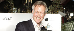 Smiling man in a suit holding an award at an indoor event, with a "Boat" banner in the background.