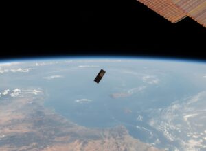 A satellite orbiting Earth over a vast ocean and landmass with part of a solar panel visible in space.