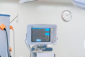 A medical monitor displaying patient vitals in a hospital room with a clock on the wall.
