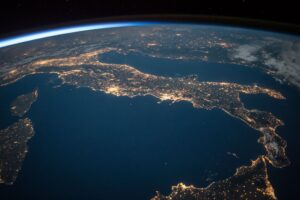 A view of Earth from space at night, showing Italy illuminated with city lights under a dark sky.