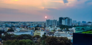Panoramic view of a cityscape at sunset, with the sun setting behind high-rise buildings and colorful sky.