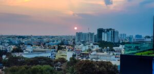 Cityscape at sunset with a glowing sun, high-rise buildings, and a colorful sky.