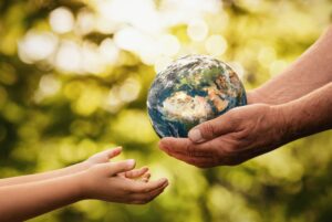 Child's hands reaching for a small globe held by an adult, against a blurred green nature background.