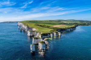 Aerial view of chalk cliffs with green fields on top, surrounded by blue sea under a clear sky.