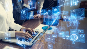 Person typing on a laptop surrounded by digital holograms and charts, with business documents on a wooden table.