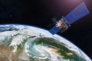 A satellite orbits above Earth, with solar panels extended, against a backdrop of swirling clouds and land.